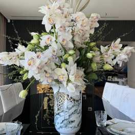 Large white orchid arrangement in a decorative vase on a dining table