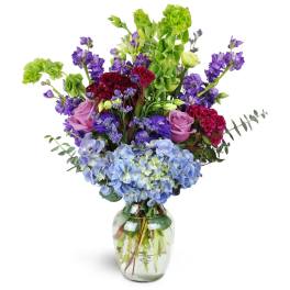 Mixed bouquet of purple, pink, blue, and green flowers in a glass vase