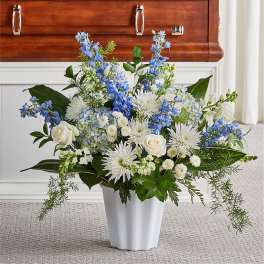 Tall blue and white sympathy arrangement with roses and delphinium in a white vase