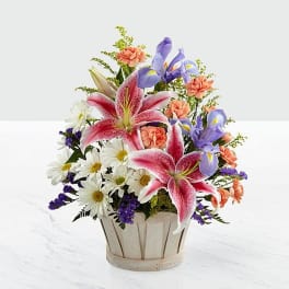Mixed bouquet in a wooden basket with pink lilies, irises, daisies, and carnations
