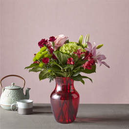 Mixed bouquet in a red glass vase with a teapot and mug beside it