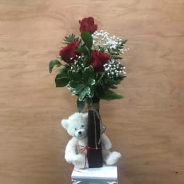 Red roses in a tall vase with a white teddy bear