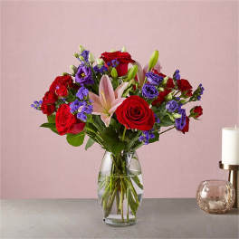 Bouquet of red roses, purple blooms, and a pink lily in a glass vase