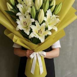 Bouquet of white lilies wrapped in bright yellow paper with a white ribbon