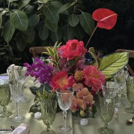 Tropical floral centerpiece with pink and purple blooms on a table set with glassware