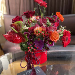 Bright mixed flower arrangement in a red hat box with roses and gerbera daisies