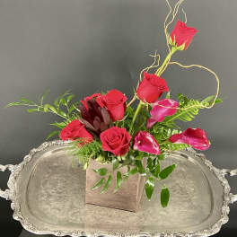 Red roses and pink calla lilies arranged in a square wooden vase