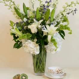 White lilies and roses in a glass vase with kiwi and a teacup