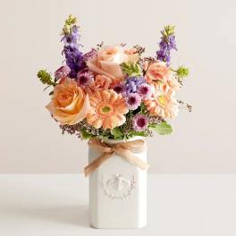 Peach and purple flower arrangement in a white vase with a ribbon
