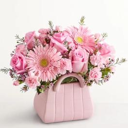 Pink roses and gerbera daisies in a pink handbag-shaped vase