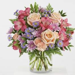 Bouquet of peach roses, pink alstroemeria, and purple daisies in a glass vase