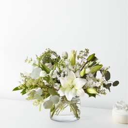 White lilies and mixed white flowers in a clear glass vase