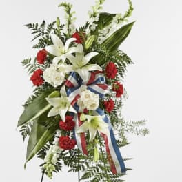 Standing floral spray with white lilies, red carnations, and a red-white-blue ribbon