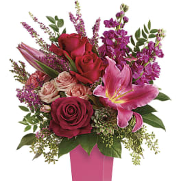 Tall arrangement of red roses, pink lilies, and mixed blooms in a bright pink vase