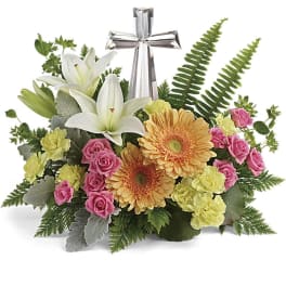 Low arrangement of pastel lilies, gerbera daisies, roses, and carnations around a clear crystal cross.