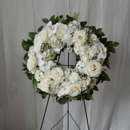 White floral wreath on a black stand with roses and orchids