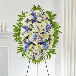 Standing floral spray with white lilies, roses, and purple accents on an easel
