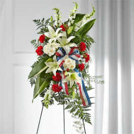 Standing floral spray with white lilies, red carnations, and ribbon on an easel