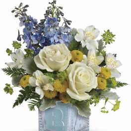 Bouquet of white roses, blue flowers, and yellow blooms in a glass cube vase