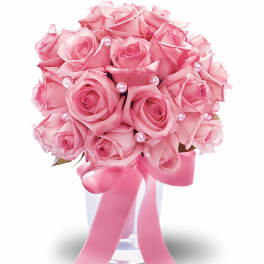 Compact arrangement of pink roses in a clear vase with pink ribbon and pearl accents
