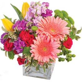 Mixed bouquet with pink gerberas, roses, tulips, and purple blooms in a glass vase