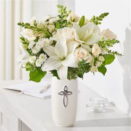 White lilies and cream roses in a white vase with a cross