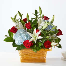 Basket arrangement of red roses, white lilies, and blue hydrangeas