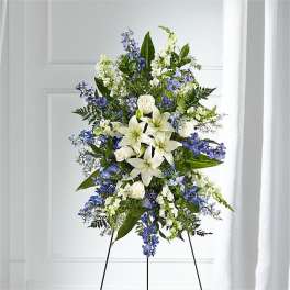 Standing floral spray with white lilies and blue flowers on an easel