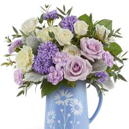 Lavender and white roses and mums arranged in a blue daisy-print ceramic pitcher