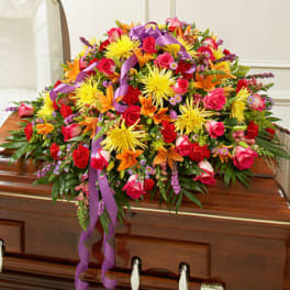Bright multicolor casket spray with roses, lilies, and mums on a wooden casket.