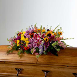 Colorful mixed-flower casket spray with lilies, roses, and sunflowers on a wooden coffin