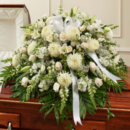 Large white funeral casket spray with roses, lilies, and ribbons on a wood casket