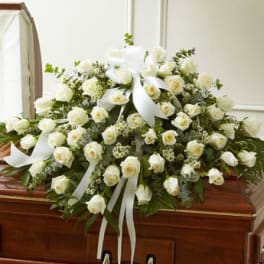 Large white rose casket spray with white ribbons on a wooden casket