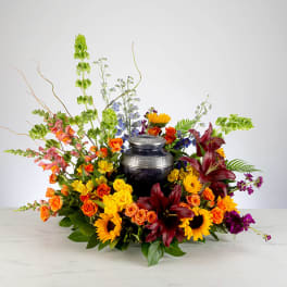 Colorful cremation floral arrangement of sunflowers, roses, and lilies surrounding a decorative urn