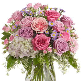 Pink and lavender rose bouquet with white hydrangea and purple asters in a clear glass vase