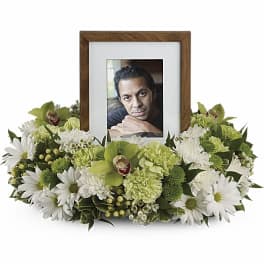 Low ring of white and green flowers surrounding a wooden picture frame with a portrait.