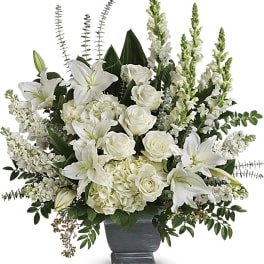 Tall arrangement of white lilies, roses, hydrangeas, and snapdragons in a gray pedestal vase