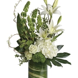 Tall white and green arrangement with lilies, hydrangeas, and roses in a clear glass cylinder vase