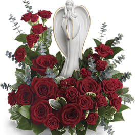 Red rose arrangement surrounding a white ceramic praying angel figurine