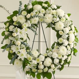 Large white floral wreath with lilies and roses on a metal easel with a white ribbon