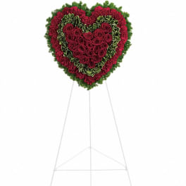 Heart-shaped standing arrangement of red roses and carnations with green accents on a white easel