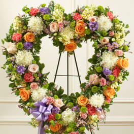 Heart-shaped standing wreath of mixed roses, carnations, and mums with lavender bow on an easel