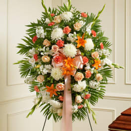 Standing sympathy spray of white, peach, and orange flowers with ribbon on an easel