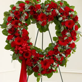 Heart-shaped standing wreath of red roses, carnations, and gerbera daisies with white filler flowers
