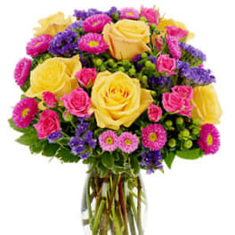 Vase arrangement of yellow roses with pink and purple flowers in a clear glass vase
