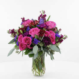 Pink roses and purple flowers arranged in a clear glass vase