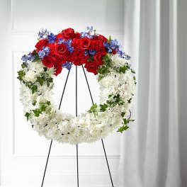 Circular funeral wreath of red, white, and blue flowers on a black stand
