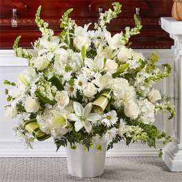 White floral arrangement in a white vase with lilies, roses, and daisies