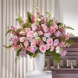 Pink and white floral arrangement in a white urn beside a casket
