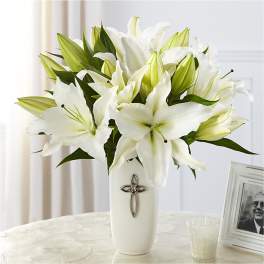 White lilies arranged in a tall white vase with a cross emblem